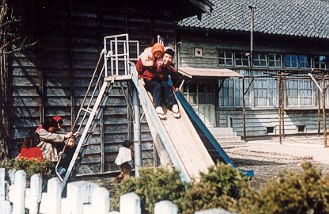 Children at wooden schoolhouse playing on slides